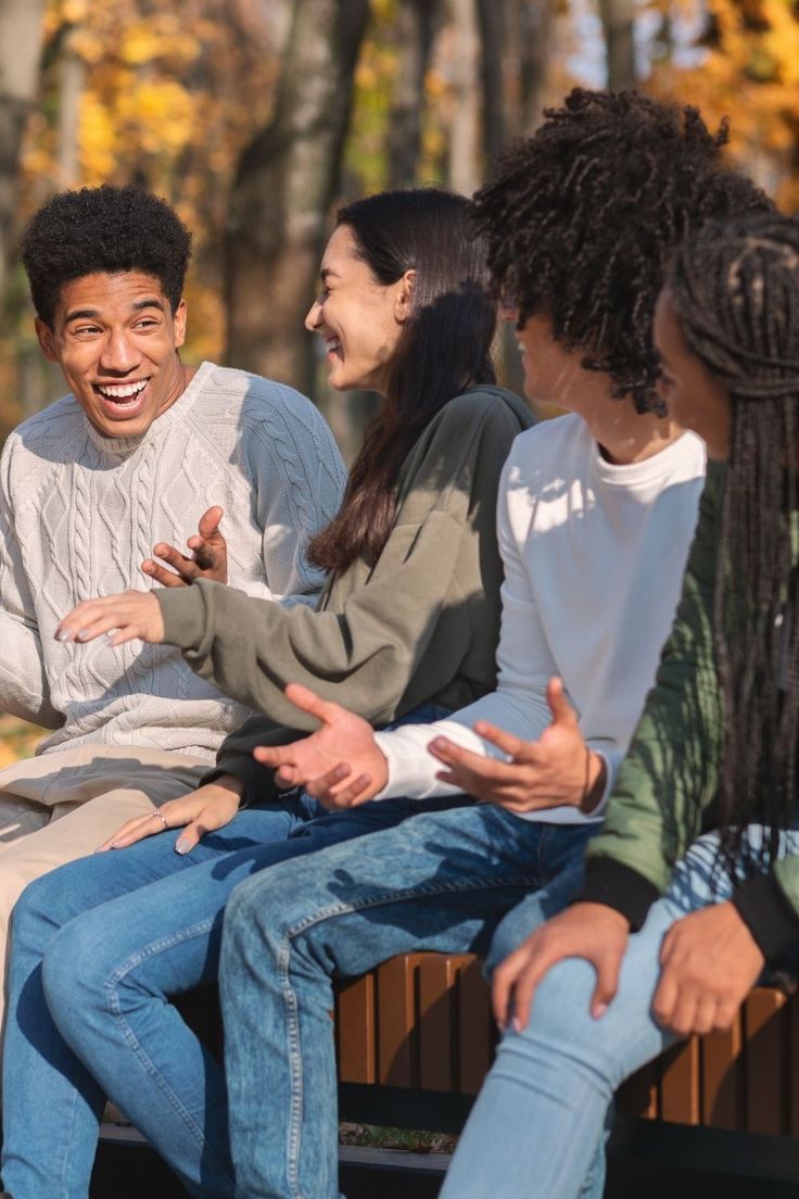 Four friends sitting on a park bench in autumn, laughing and deep in conversation.